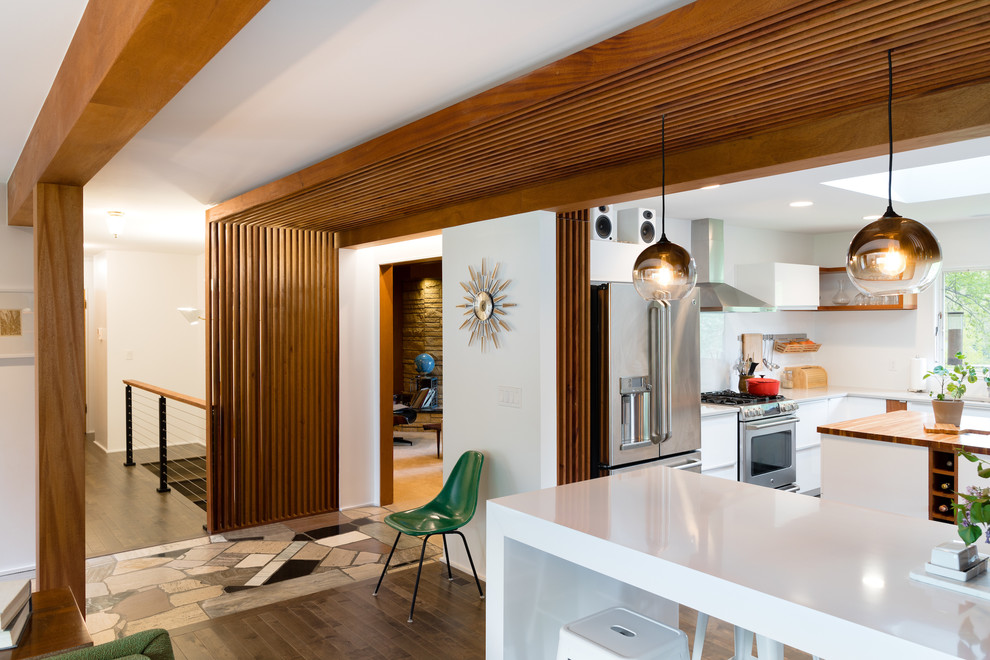 Photo of a mid-sized midcentury l-shaped open plan kitchen in Omaha with a double-bowl sink, flat-panel cabinets, white cabinets, laminate benchtops, white splashback, stainless steel appliances, dark hardwood floors, multiple islands and black floor.