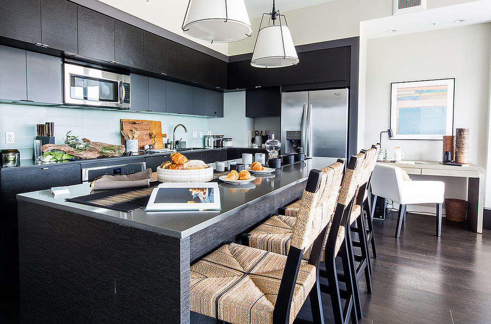 Penthouse Decor in Bethesda - Mid-sized transitional l-shaped dark wood floor and black floor open concept kitchen photo in DC Metro with an undermount sink, flat-panel cabinets, black cabinets, solid surface countertops, white backsplash, glass tile backsplash, stainless steel appliances and an island