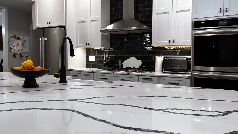 Large transitional single-wall vinyl floor and beige floor eat-in kitchen photo with a farmhouse sink, shaker cabinets, white cabinets, quartz countertops, black backsplash, subway tile backsplash, stainless steel appliances, an island and white countertops