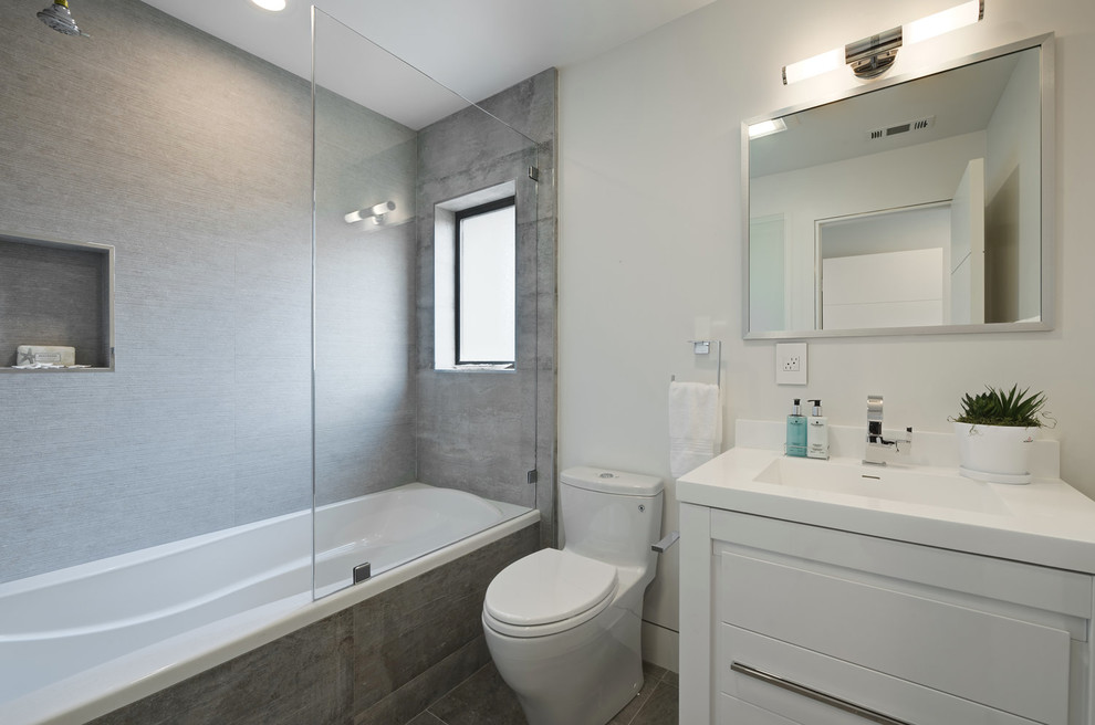Photo of a mid-sized transitional 3/4 bathroom in San Francisco with flat-panel cabinets, white cabinets, an alcove tub, a shower/bathtub combo, an integrated sink, a one-piece toilet, gray tile, porcelain tile and white walls.