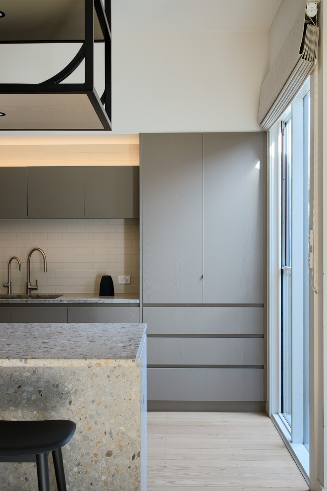 This is an example of a small contemporary single-wall kitchen in Melbourne with flat-panel cabinets, grey cabinets, terrazzo benchtops, light hardwood floors, with island and multi-coloured benchtop.