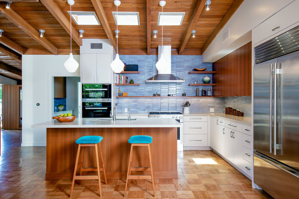 Large midcentury l-shaped open plan kitchen in Los Angeles with an undermount sink, flat-panel cabinets, medium wood cabinets, quartz benchtops, blue splashback, ceramic splashback, stainless steel appliances, light hardwood floors, with island and grey benchtop.