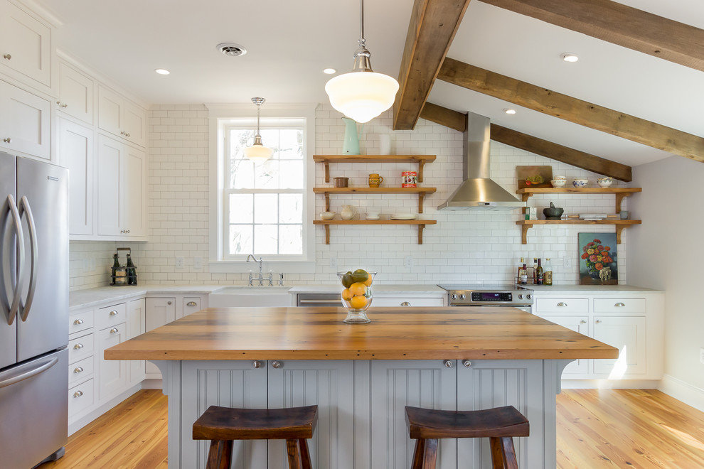 This is an example of a large country l-shaped kitchen in DC Metro with a farmhouse sink, shaker cabinets, white cabinets, marble benchtops, white splashback, subway tile splashback, stainless steel appliances, light hardwood floors and with island.