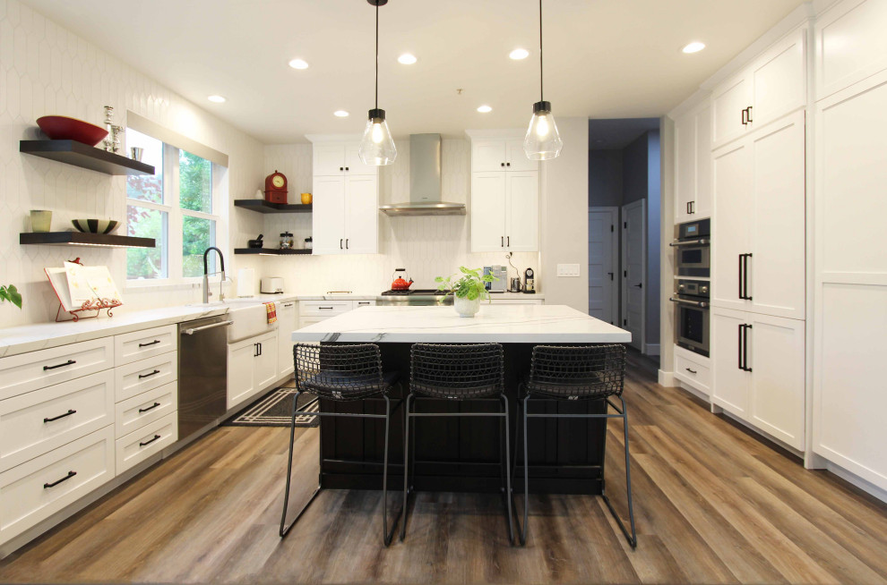 Inspiration for a large transitional l-shaped vinyl floor and brown floor open concept kitchen remodel with a farmhouse sink, shaker cabinets, white cabinets, quartz countertops, white backsplash, ceramic backsplash, stainless steel appliances, an island and white countertops