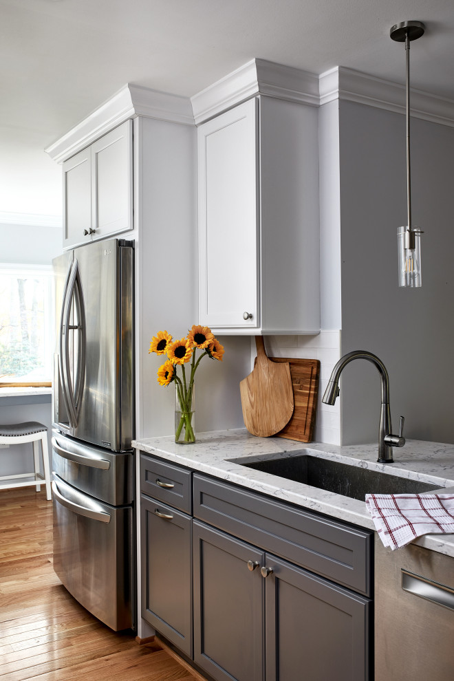 This is an example of a mid-sized transitional l-shaped eat-in kitchen in Chicago with an undermount sink, recessed-panel cabinets, white cabinets, quartz benchtops, white splashback, ceramic splashback, stainless steel appliances, medium hardwood floors, a peninsula, brown floor and grey benchtop.