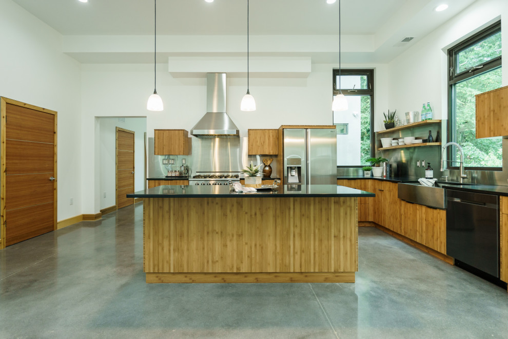 Design ideas for a contemporary l-shaped kitchen in Raleigh with a farmhouse sink, flat-panel cabinets, medium wood cabinets, metallic splashback, stainless steel appliances, concrete floors, with island, grey floor and black benchtop.