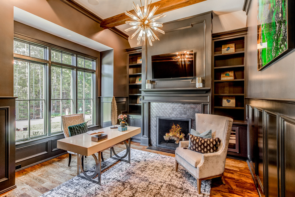 Design ideas for a transitional home office in Raleigh with grey walls, medium hardwood floors, a standard fireplace, a tile fireplace surround and brown floor.