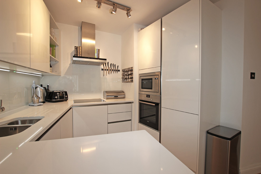 This is an example of a small modern kitchen in London with white cabinets, flat-panel cabinets, stainless steel appliances and a peninsula.