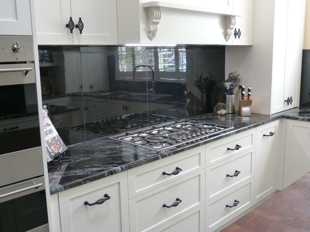 Design ideas for a mid-sized traditional u-shaped separate kitchen in Adelaide with a double-bowl sink, shaker cabinets, white cabinets, granite benchtops, black splashback, glass tile splashback, white appliances, slate floors, with island, black floor and black benchtop.