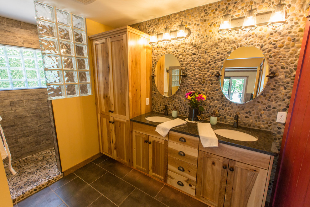 Photo of a mid-sized country master bathroom in Minneapolis with flat-panel cabinets, medium wood cabinets, an open shower, a two-piece toilet, multi-coloured tile, pebble tile, multi-coloured walls, ceramic floors, an undermount sink, granite benchtops, grey floor and an open shower.