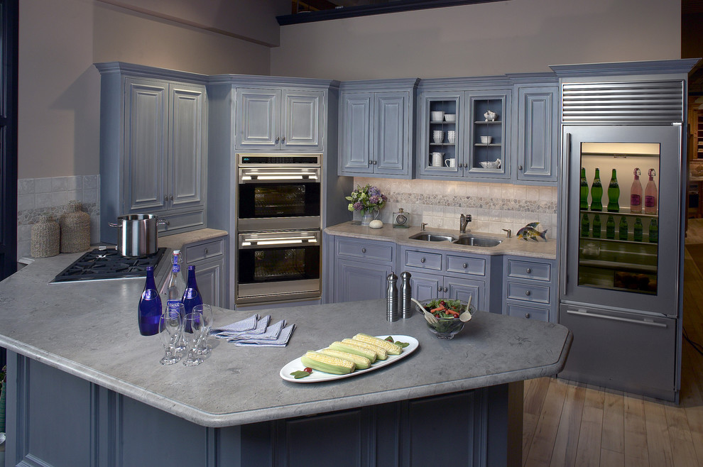 Inspiration for a mid-sized transitional l-shaped separate kitchen in Boston with a double-bowl sink, blue cabinets, raised-panel cabinets, soapstone benchtops, white splashback, ceramic splashback, stainless steel appliances, light hardwood floors and a peninsula.
