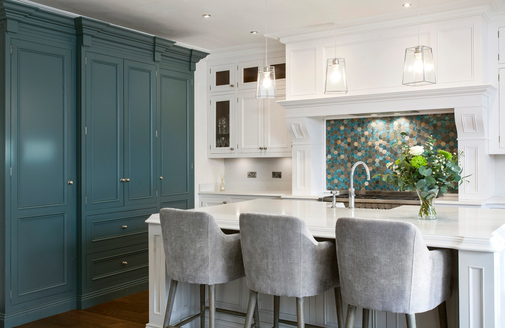 This is an example of a medium sized traditional grey and teal l-shaped kitchen/diner in Other with beaded cabinets, white cabinets, an island, a belfast sink, marble worktops, multi-coloured splashback, stainless steel appliances, dark hardwood flooring, brown floors and white worktops.