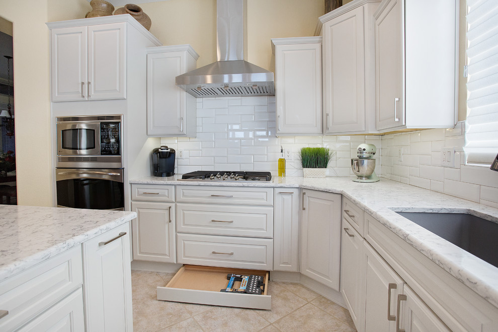 Inspiration for a mid-sized transitional single-wall ceramic tile and beige floor eat-in kitchen remodel with an undermount sink, raised-panel cabinets, white cabinets, quartz countertops, white backsplash, porcelain backsplash, stainless steel appliances and an island