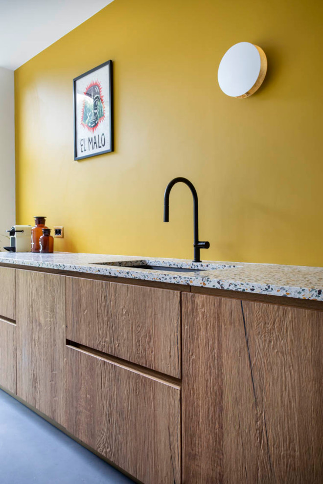 Immagine di una grande cucina con lavello sottopiano, ante a filo, ante in legno bruno, top alla veneziana, paraspruzzi giallo, elettrodomestici da incasso, pavimento in cemento, pavimento grigio e top bianco