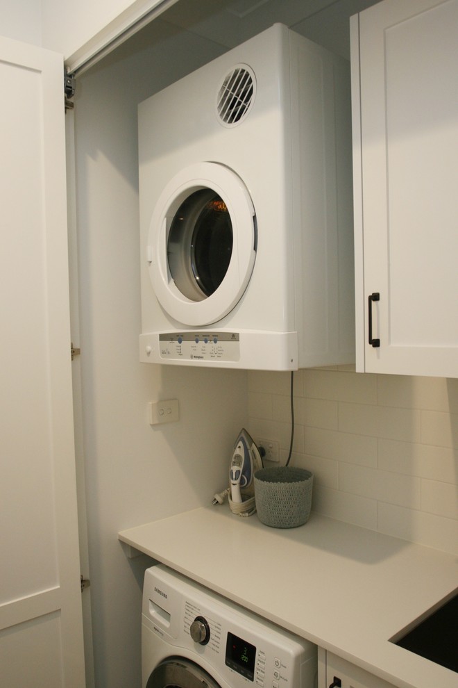 This is an example of a mid-sized traditional single-wall utility room in Sydney with an undermount sink, shaker cabinets, white cabinets, solid surface benchtops, white walls, ceramic floors, an integrated washer and dryer, multi-coloured floor and white benchtop.