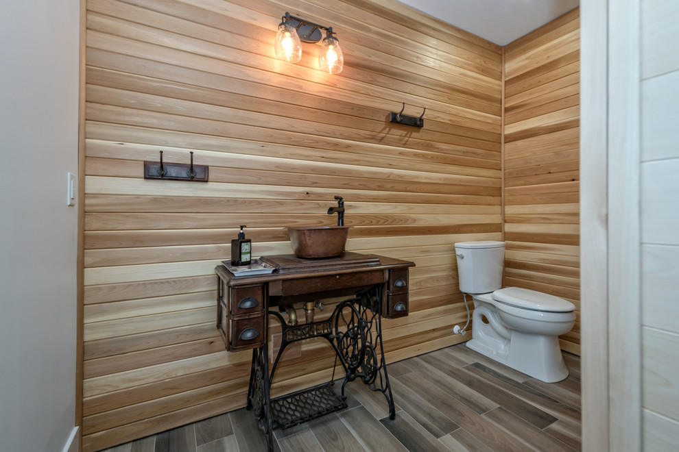 Photo of a mid-sized country powder room in Vancouver with open cabinets, black cabinets, a two-piece toilet, beige walls, porcelain floors, a vessel sink, wood benchtops and brown floor.
