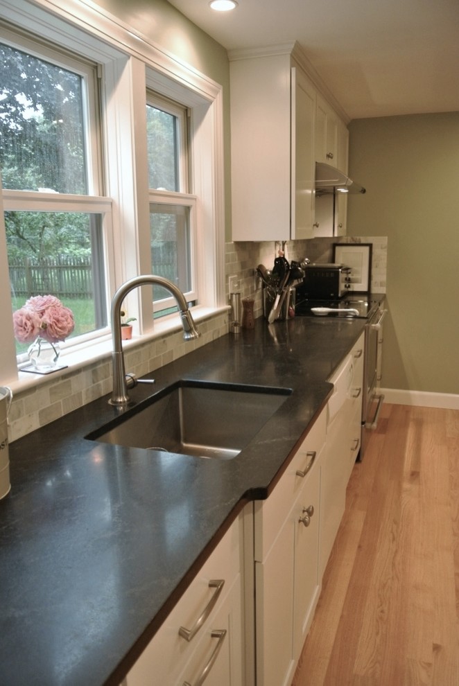 Inspiration for a transitional u-shaped light wood floor eat-in kitchen remodel in Boston with an undermount sink, shaker cabinets, white cabinets, beige backsplash, porcelain backsplash, stainless steel appliances, a peninsula and black countertops