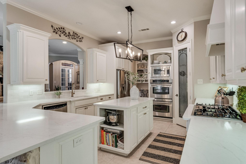 This is an example of a large traditional l-shaped eat-in kitchen in Dallas with an undermount sink, raised-panel cabinets, white cabinets, quartz benchtops, white splashback, subway tile splashback, stainless steel appliances, ceramic floors, a peninsula, beige floor and white benchtop.