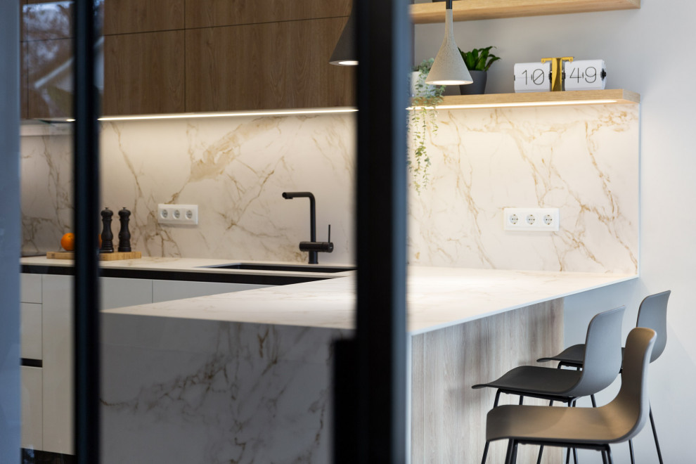 Inspiration for a large contemporary l-shaped kitchen in Barcelona with a submerged sink, flat-panel cabinets, engineered stone countertops, white splashback, engineered quartz splashback, black appliances, porcelain flooring, a breakfast bar, grey floors, white worktops and a drop ceiling.