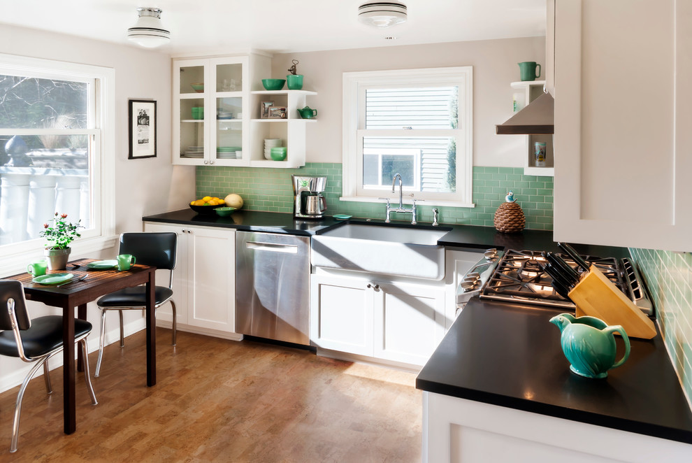 Small u-shaped eat-in kitchen in Seattle with a farmhouse sink, shaker cabinets, white cabinets, green splashback, porcelain splashback, stainless steel appliances, cork floors and no island.