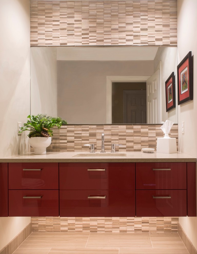 This is an example of a small contemporary powder room in New York with an undermount sink, red cabinets, solid surface benchtops, stone tile, grey walls, beige tile, flat-panel cabinets, porcelain floors, beige floor and grey benchtops.
