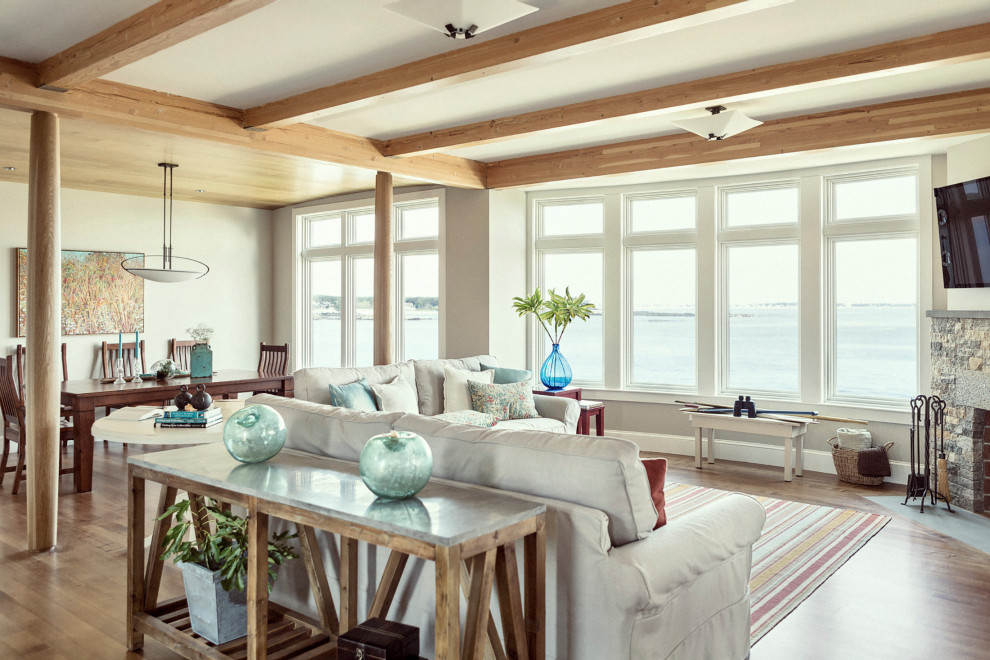 This is an example of a beach style living room in Portland Maine with white walls, medium hardwood floors, a standard fireplace, a stone fireplace surround, a wall-mounted tv and brown floor.
