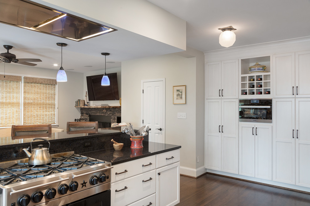 Photo of a mid-sized transitional kitchen in DC Metro with shaker cabinets, white cabinets, quartz benchtops, stainless steel appliances, dark hardwood floors, a peninsula, brown floor and black benchtop.