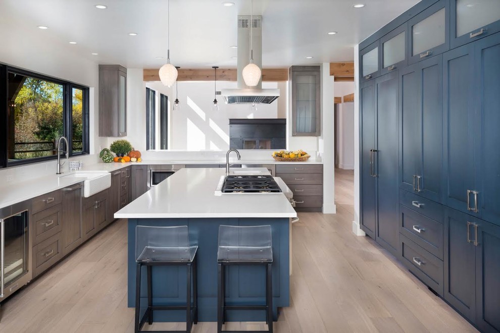 Inspiration for a large transitional l-shaped separate kitchen in Denver with blue cabinets, a farmhouse sink, shaker cabinets, window splashback, light hardwood floors, with island, beige floor, quartz benchtops, panelled appliances and white benchtop.