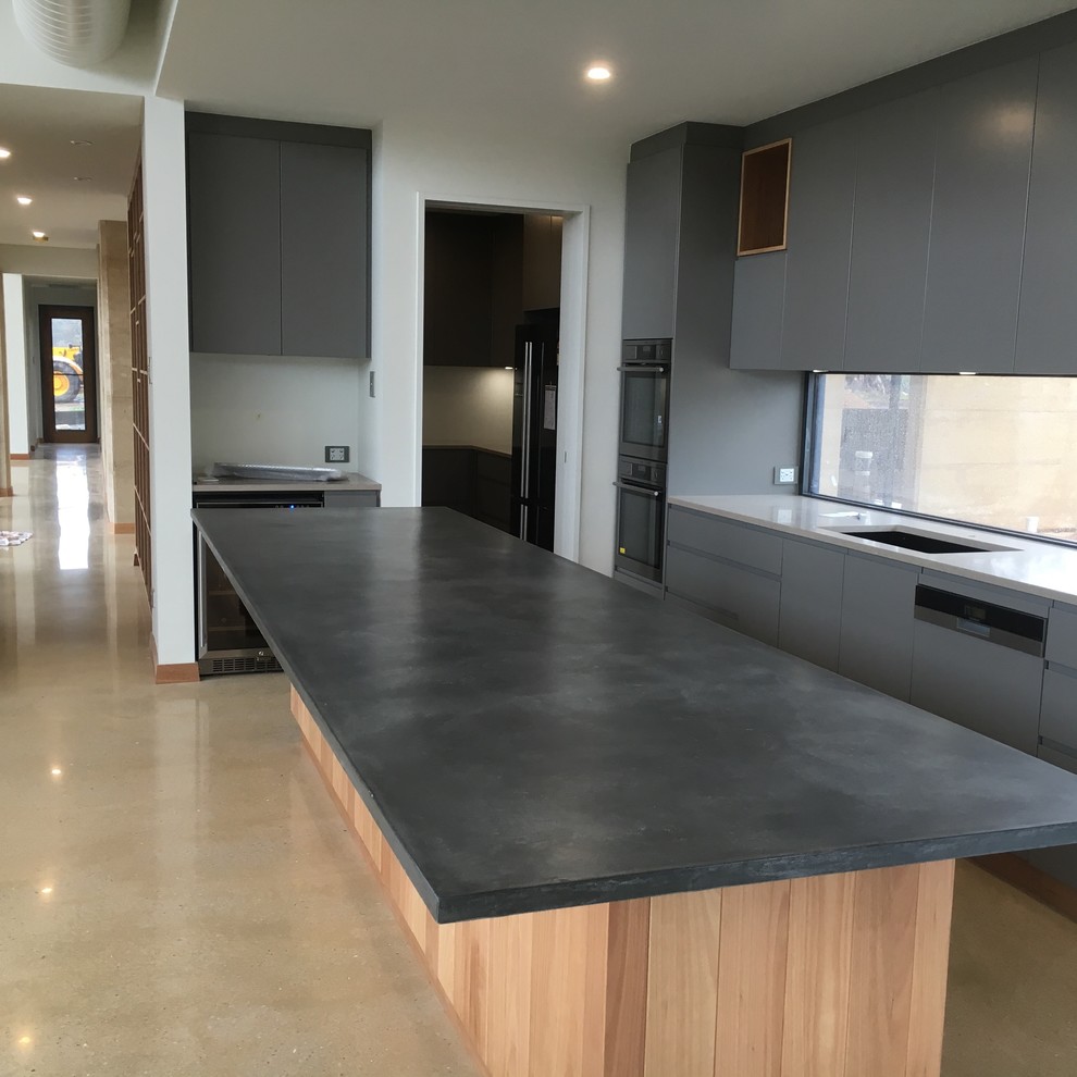Design ideas for a contemporary l-shaped kitchen in Adelaide with a single-bowl sink, flat-panel cabinets, grey cabinets, concrete benchtops, window splashback, stainless steel appliances, concrete floors, with island and beige floor.