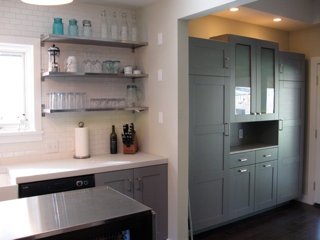 Example of a mid-sized transitional galley dark wood floor enclosed kitchen design in Seattle with a farmhouse sink, shaker cabinets, blue cabinets, quartz countertops, white backsplash, ceramic backsplash, black appliances and an island
