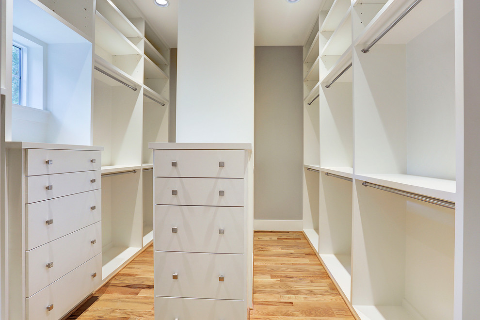 This is an example of a large modern gender-neutral walk-in wardrobe in Houston with flat-panel cabinets, white cabinets, light hardwood floors and beige floor.