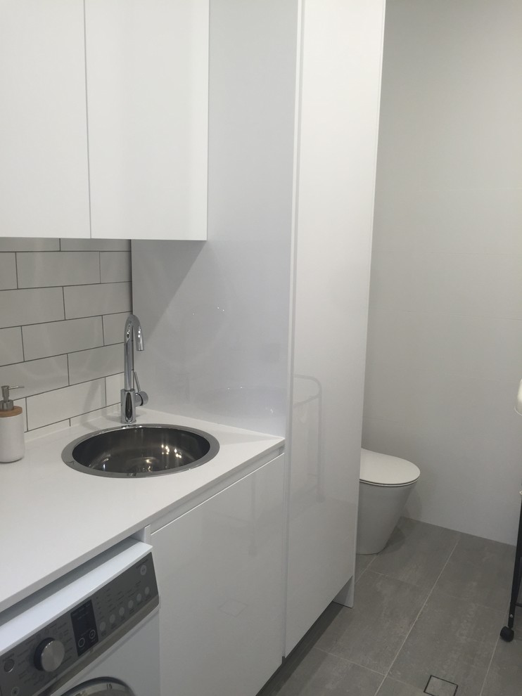 Photo of a small contemporary single-wall dedicated laundry room in Sydney with a drop-in sink, flat-panel cabinets, white cabinets, quartz benchtops, white walls, ceramic floors, a side-by-side washer and dryer and white floor.