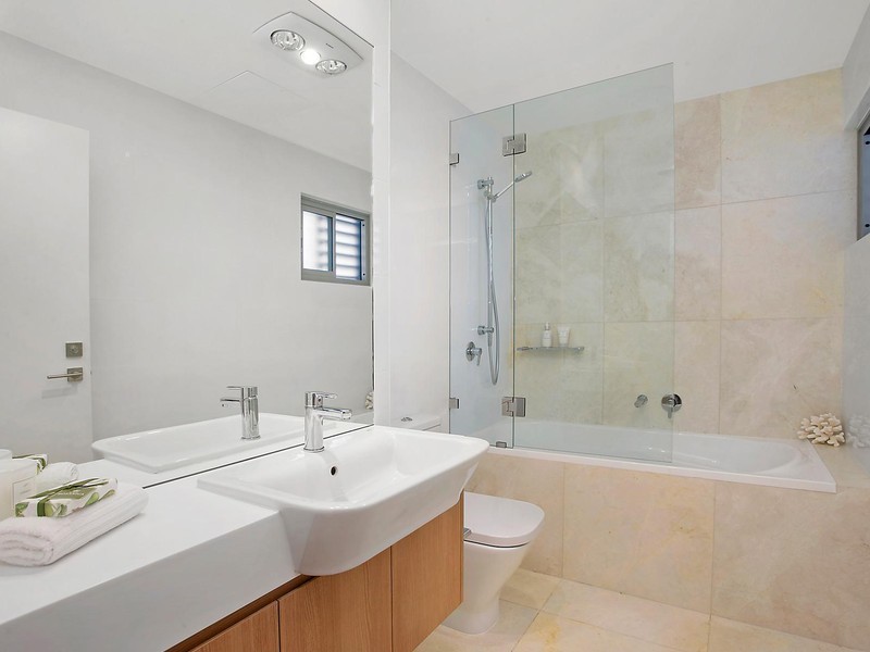 Mid-sized contemporary kids bathroom in Sydney with flat-panel cabinets, medium wood cabinets, a drop-in tub, a shower/bathtub combo, a one-piece toilet, white tile, ceramic tile, white walls, travertine floors, a drop-in sink and engineered quartz benchtops.
