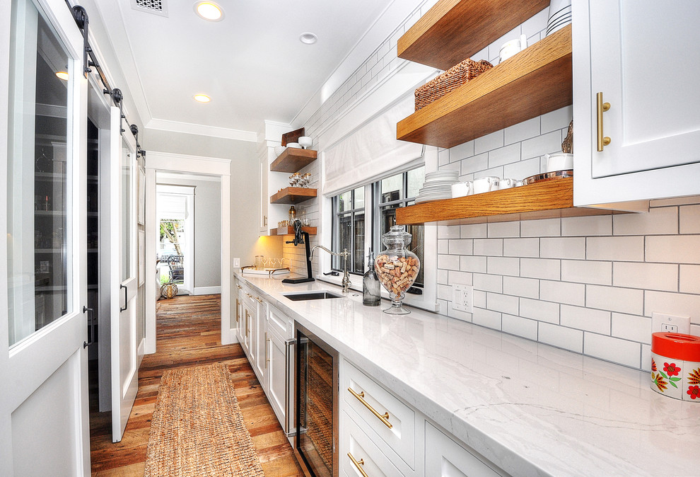 Photo of a country single-wall home bar in Orange County with an undermount sink, beaded inset cabinets, white cabinets, white splashback, subway tile splashback, medium hardwood floors and brown floor.