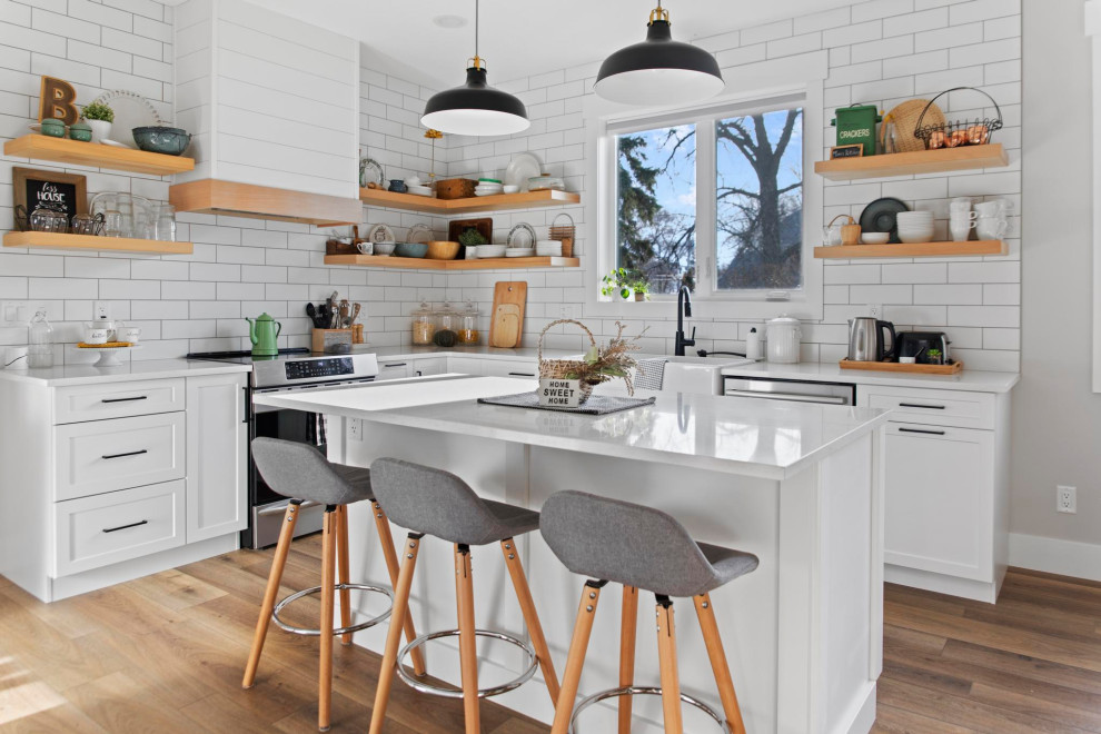 Design ideas for a country l-shaped kitchen in Edmonton with quartzite benchtops, with island, a farmhouse sink, shaker cabinets, white cabinets, white splashback, subway tile splashback, stainless steel appliances, dark hardwood floors, brown floor and white benchtop.