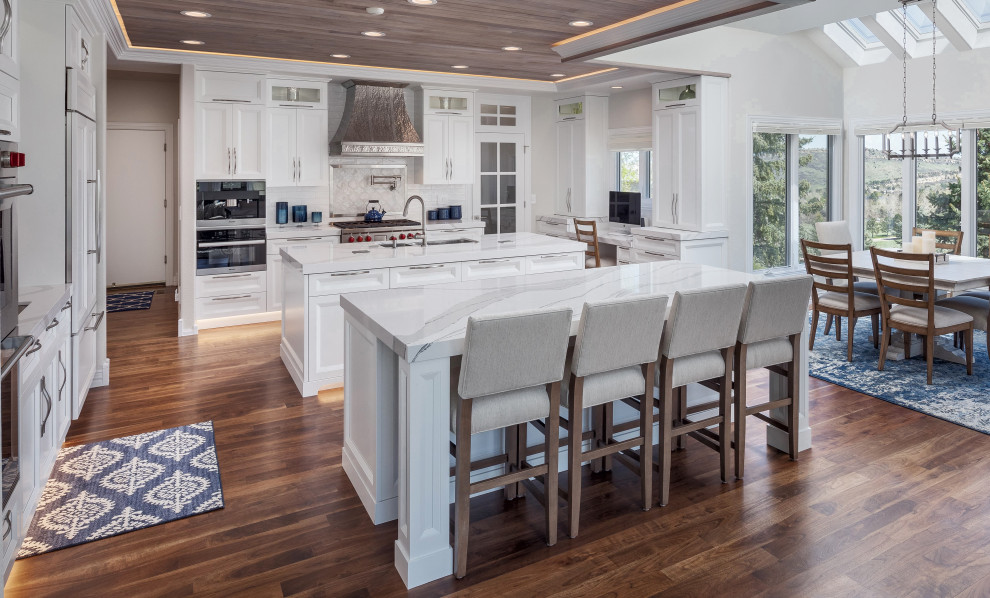 Inspiration for a large transitional eat-in kitchen in Denver with an undermount sink, shaker cabinets, white cabinets, quartz benchtops, white splashback, stainless steel appliances, medium hardwood floors, multiple islands, brown floor and white benchtop.