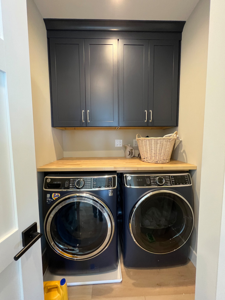 This is an example of a small beach style single-wall laundry cupboard in Other with an undermount sink, shaker cabinets, blue cabinets, wood benchtops, white walls, laminate floors, a side-by-side washer and dryer, brown floor and brown benchtop.
