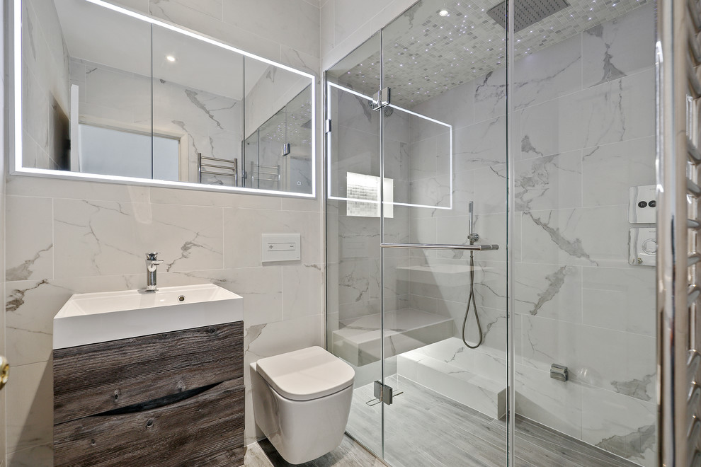 Photo of a small contemporary 3/4 bathroom in Surrey with flat-panel cabinets, dark wood cabinets, a curbless shower, a wall-mount toilet, gray tile, white tile, grey walls, grey floor, a console sink and a hinged shower door.