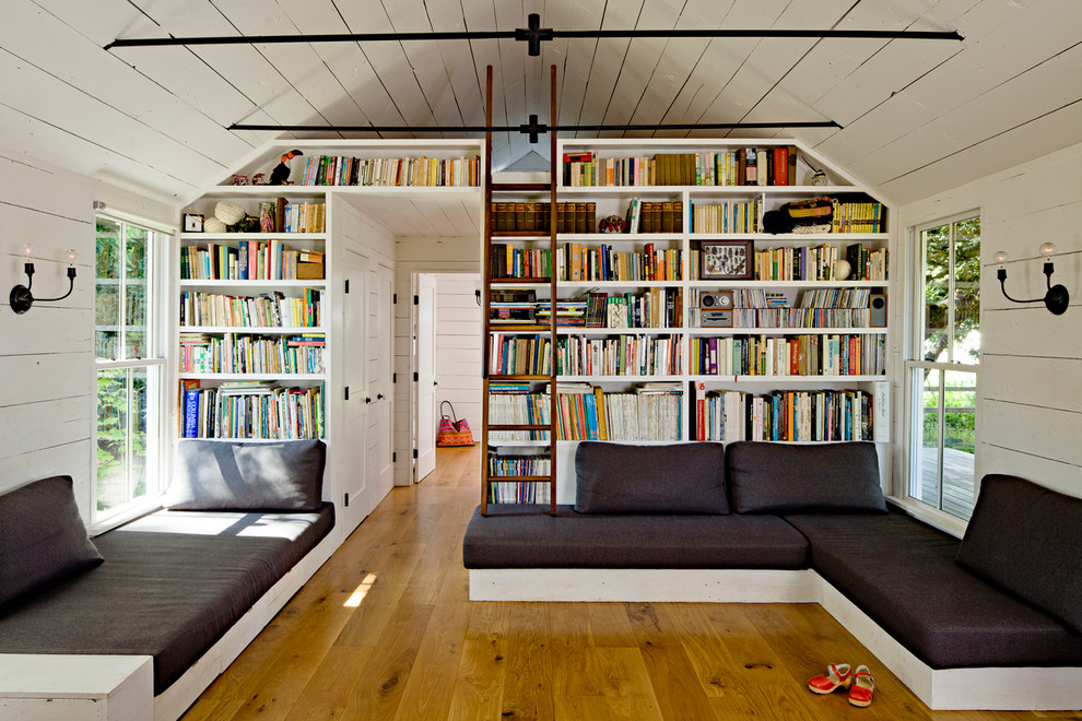 Country living room in Portland with a library, white walls and medium hardwood floors.