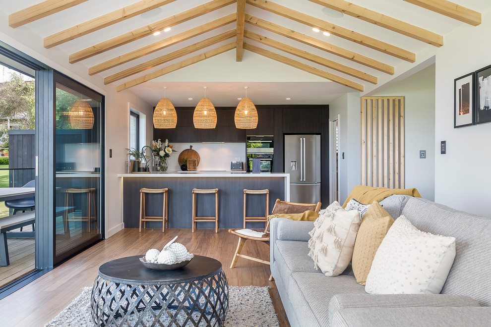 Photo of a Mid-sized beach style U-shaped open plan kitchen in Auckland With an Undermount Sink, Flat-panel Cabinets, Dark Wood Cabinets, Quartz Benchtops, White Splashback, Porcelain Splashback, Stainless Steel Appliances, Light Hardwood Floors, a Peninsula and White Benchtop.
