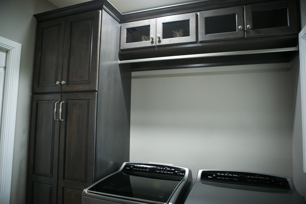 Photo of a small transitional galley dedicated laundry room in Indianapolis with an undermount sink, raised-panel cabinets, dark wood cabinets, grey walls, medium hardwood floors, a side-by-side washer and dryer, brown floor and white benchtop.