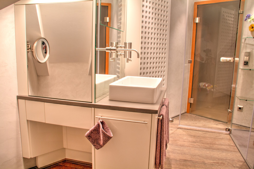 Idéer för mellanstora funkis grått badrum med dusch, med skåp i shakerstil, grå skåp, en kantlös dusch, en vägghängd toalettstol, grå kakel, grå väggar, laminatgolv, ett fristående handfat, träbänkskiva, brunt golv och dusch med gångjärnsdörr