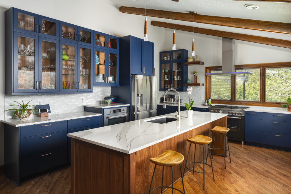 Пример оригинального дизайна: угловая кухня-гостиная среднего размера в стиле ретро с врезной мойкой, стеклянными фасадами, синими фасадами, столешницей из кварцевого агломерата, разноцветным фартуком, черной техникой, паркетным полом среднего тона, островом, белой столешницей, сводчатым потолком и двухцветным гарнитуром