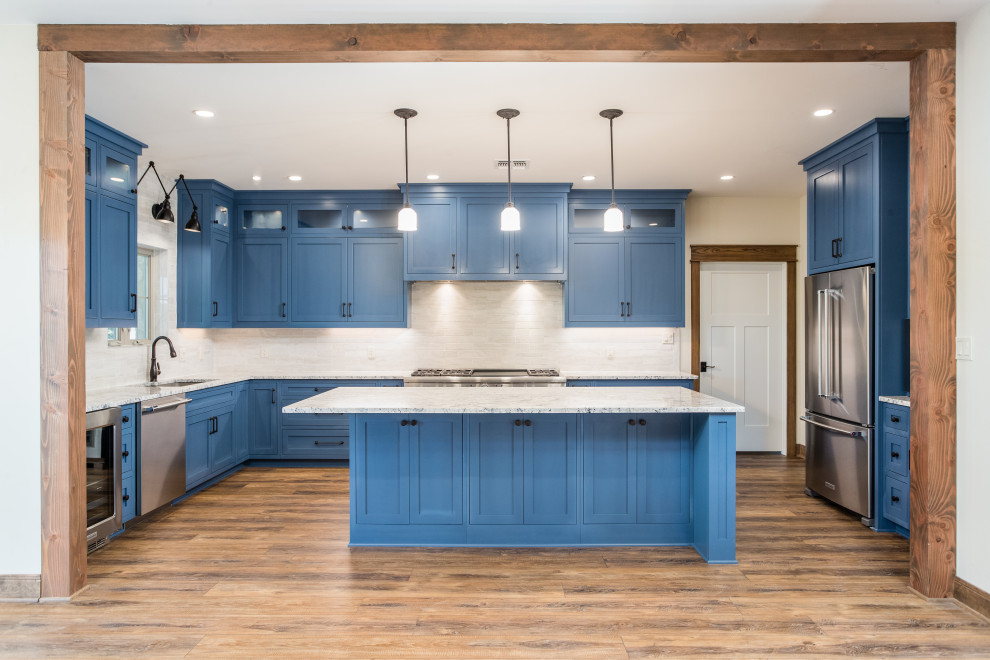 This is an example of a mid-sized country u-shaped open plan kitchen in Austin with an undermount sink, shaker cabinets, blue cabinets, granite benchtops, white splashback, porcelain splashback, stainless steel appliances, vinyl floors, with island, brown floor and blue benchtop.