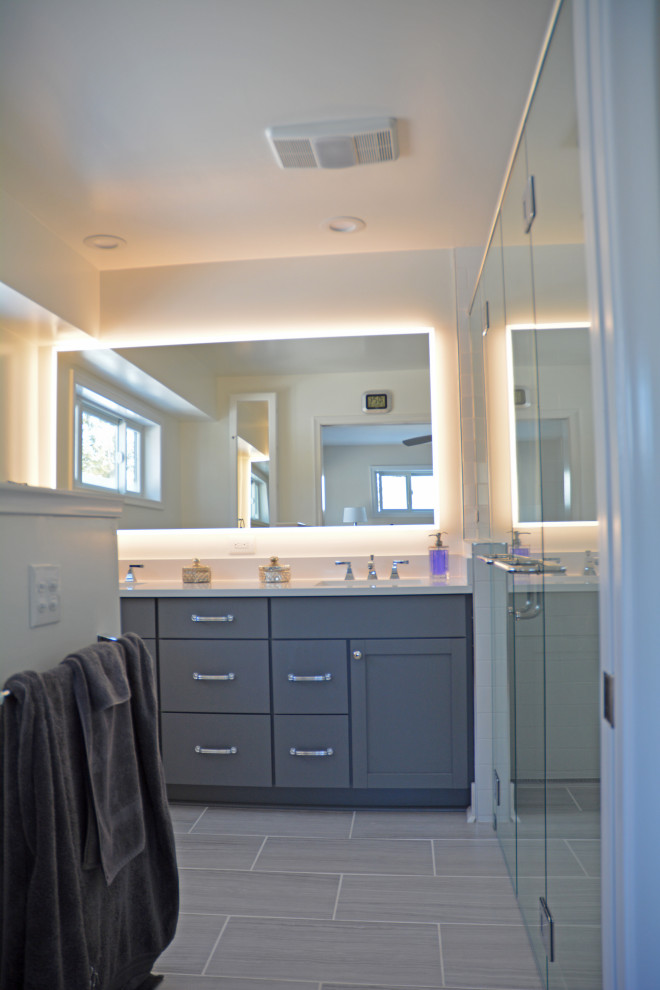 Inspiration for a large transitional master gray tile and porcelain tile porcelain tile, gray floor and double-sink walk-in shower remodel with shaker cabinets, gray cabinets, a two-piece toilet, white walls, an undermount sink, quartz countertops, a hinged shower door, white countertops, a niche and a built-in vanity