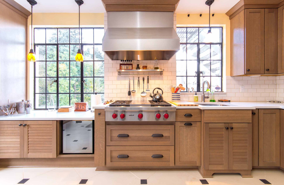 Example of a transitional l-shaped porcelain tile and white floor enclosed kitchen design in Portland with an undermount sink, shaker cabinets, light wood cabinets, solid surface countertops, white backsplash, ceramic backsplash, stainless steel appliances, an island and white countertops