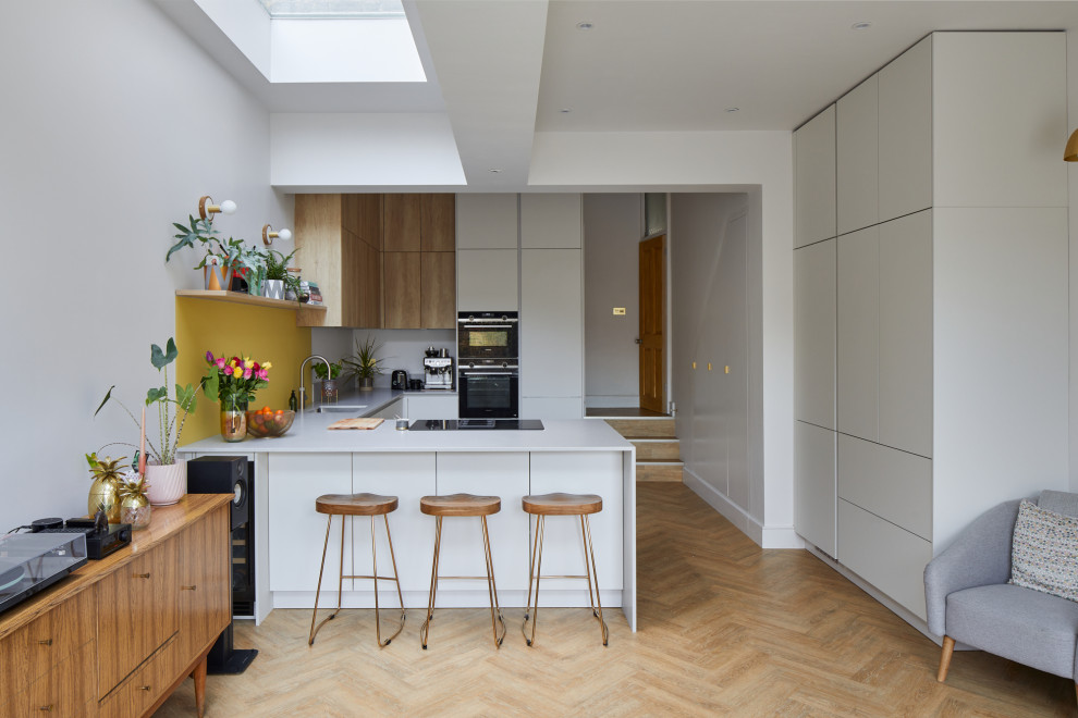 Foto på ett litet funkis vit kök, med en undermonterad diskho, släta luckor, vita skåp, bänkskiva i kvarts, gult stänkskydd, glaspanel som stänkskydd, rostfria vitvaror, mellanmörkt trägolv, en halv köksö och brunt golv
