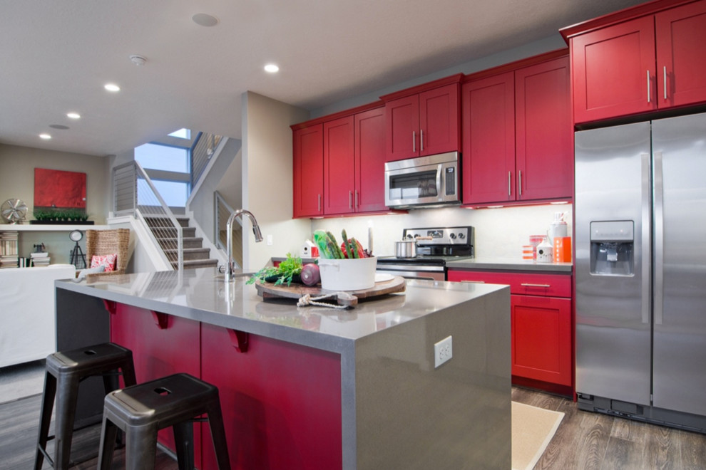 Mid-sized transitional galley open plan kitchen in Salt Lake City with white splashback, stainless steel appliances, a single-bowl sink, shaker cabinets, red cabinets, vinyl floors, with island and solid surface benchtops.