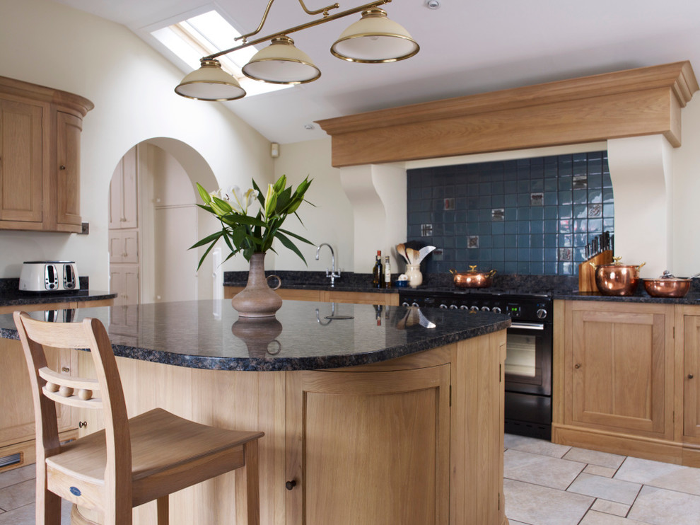 This is an example of a large traditional u-shaped open plan kitchen in Devon with a double-bowl sink, shaker cabinets, light wood cabinets, granite benchtops, blue splashback, ceramic splashback, black appliances, limestone floors and with island.