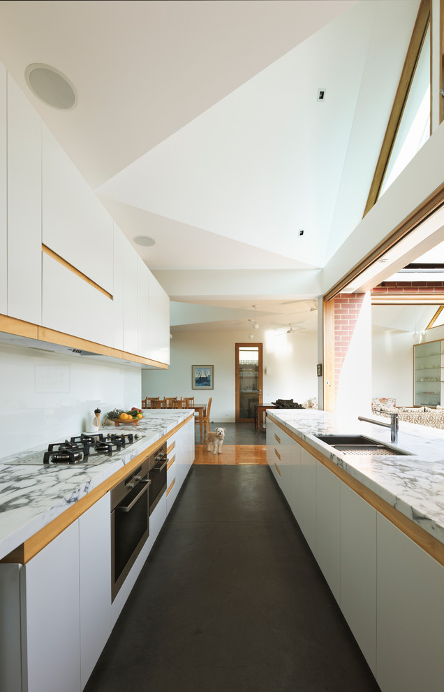 Inspiration for an expansive contemporary galley open plan kitchen in Melbourne with stainless steel appliances, an undermount sink, flat-panel cabinets, white cabinets, marble benchtops, white splashback, glass sheet splashback, concrete floors and no island.